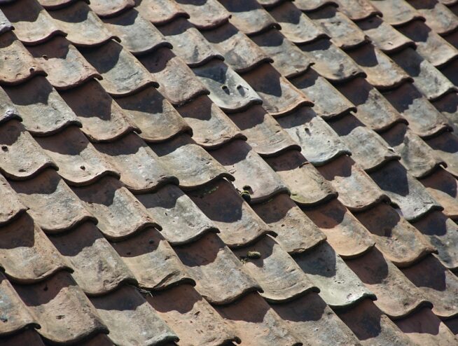 Old ceramic roof tiles with a wavy pattern and aged texture. Roof Maintenance