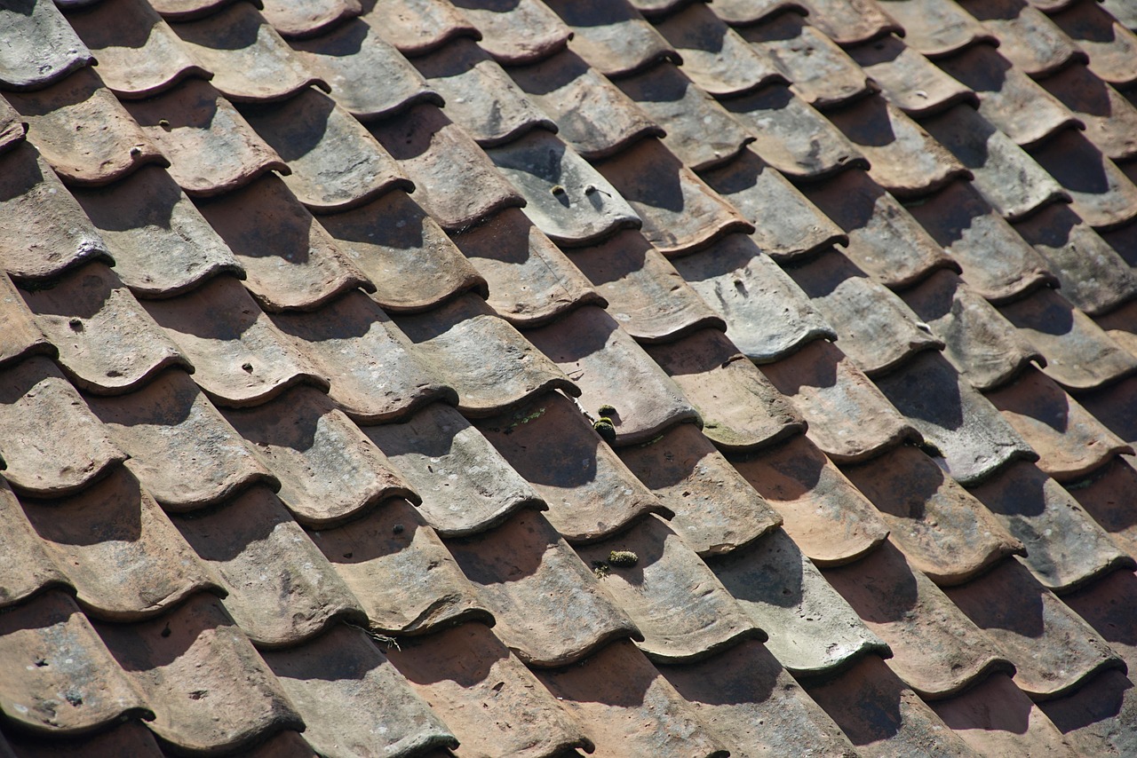 Old ceramic roof tiles with a wavy pattern and aged texture. Roof Maintenance