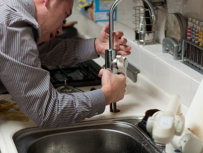 Person fixing kitchen sink, concept: cost comparison DIY vs professional plumbing repairs.