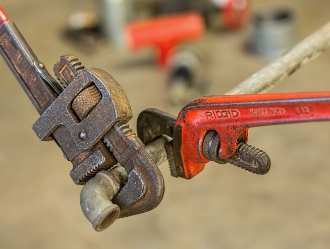 Two pipe wrenches grip a pipe, illustrating tools often involved in plumbing repair costs.