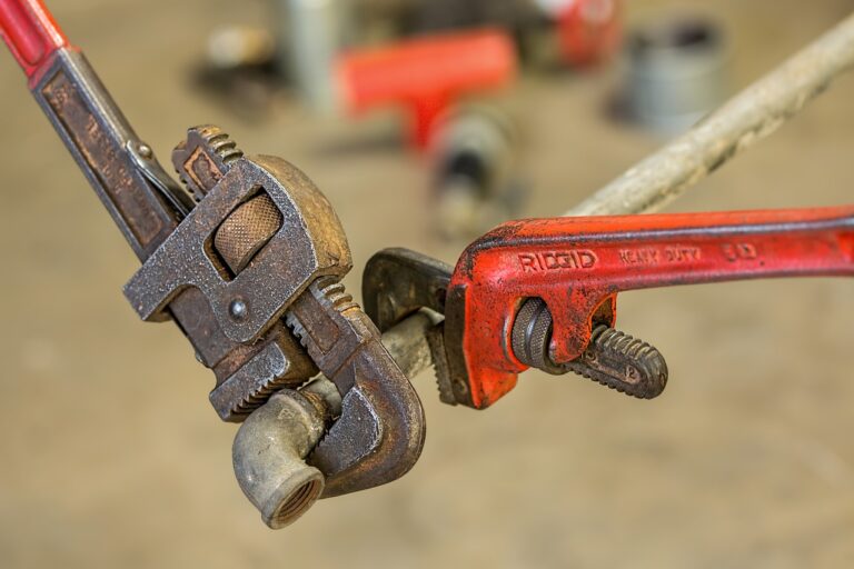 Two pipe wrenches grip a pipe, illustrating tools often involved in plumbing repair costs.